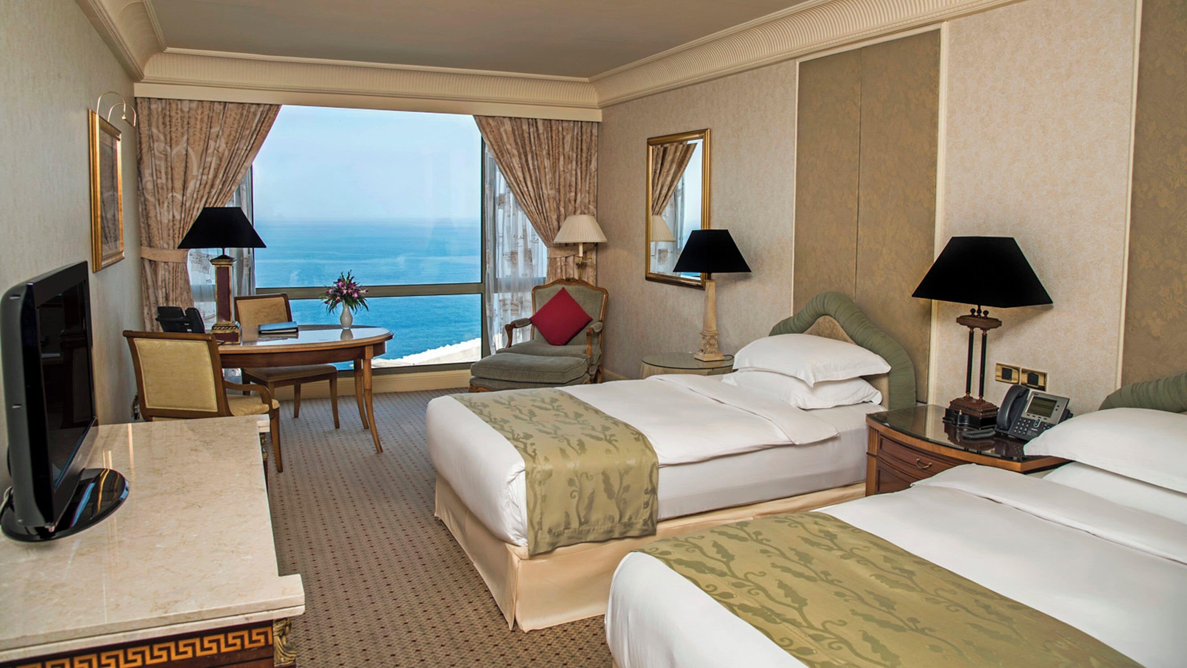 Habitación de hotel con dos camas, un escritorio, una silla, un televisor y vista al mar.