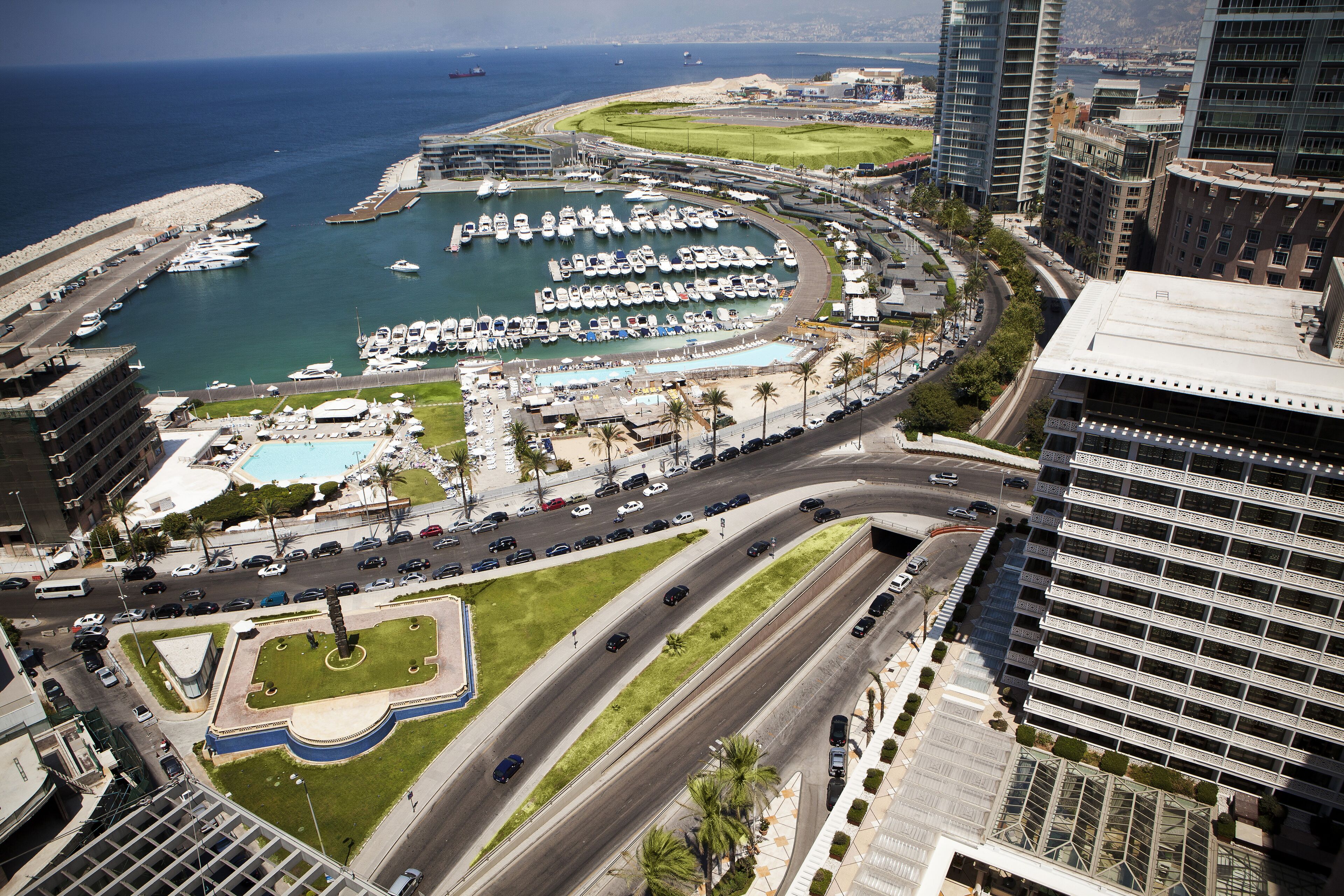 A marina with boats, a road with cars, and high-rise buildings.