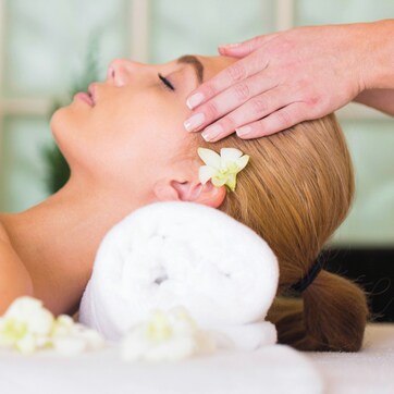 A person lying on a massage table with a white towel, receiving a head massage.