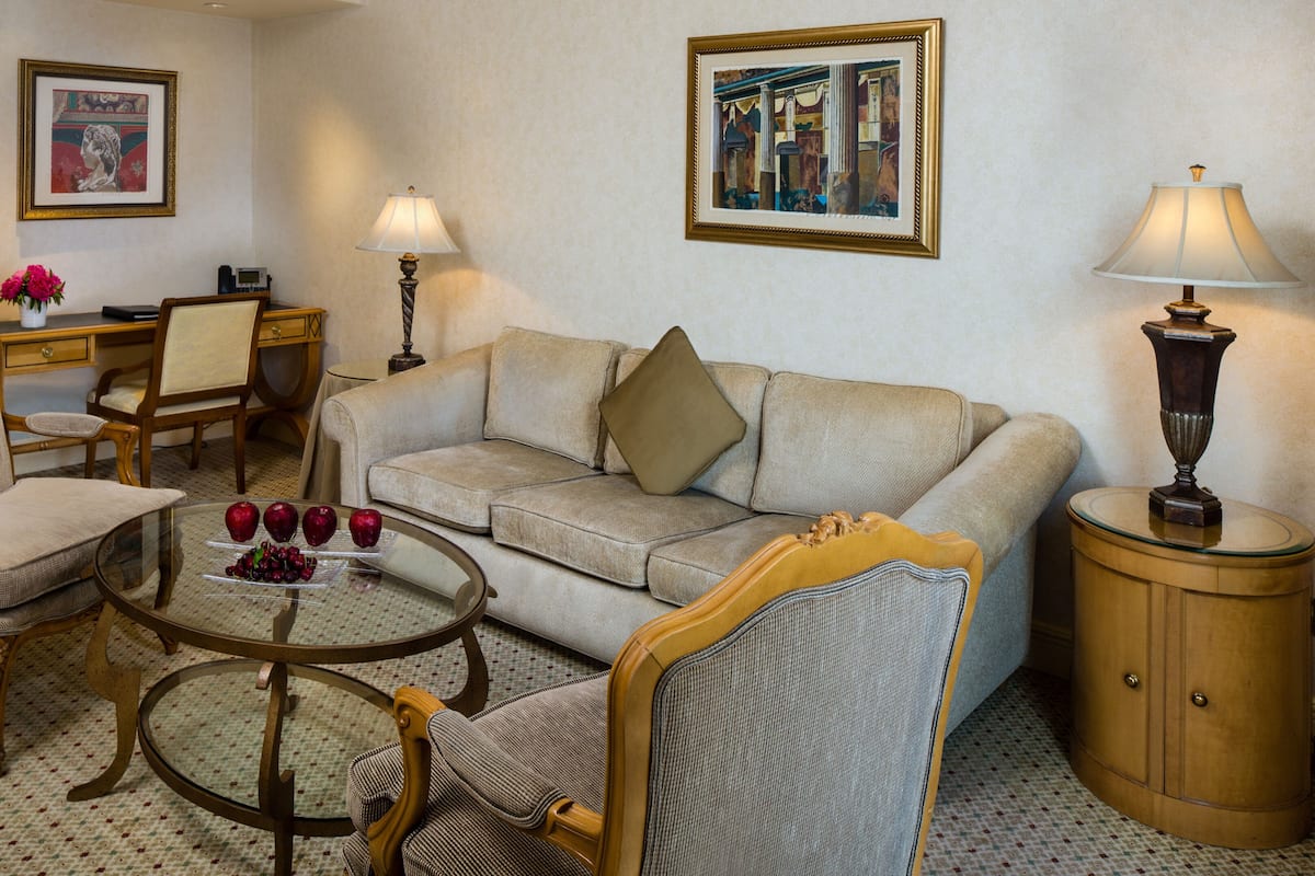 Un salon avec un canapé, des fauteuils, une table basse sur laquelle se trouvent des fruits, une lampe et des œuvres d’art encadrées accrochées aux murs.