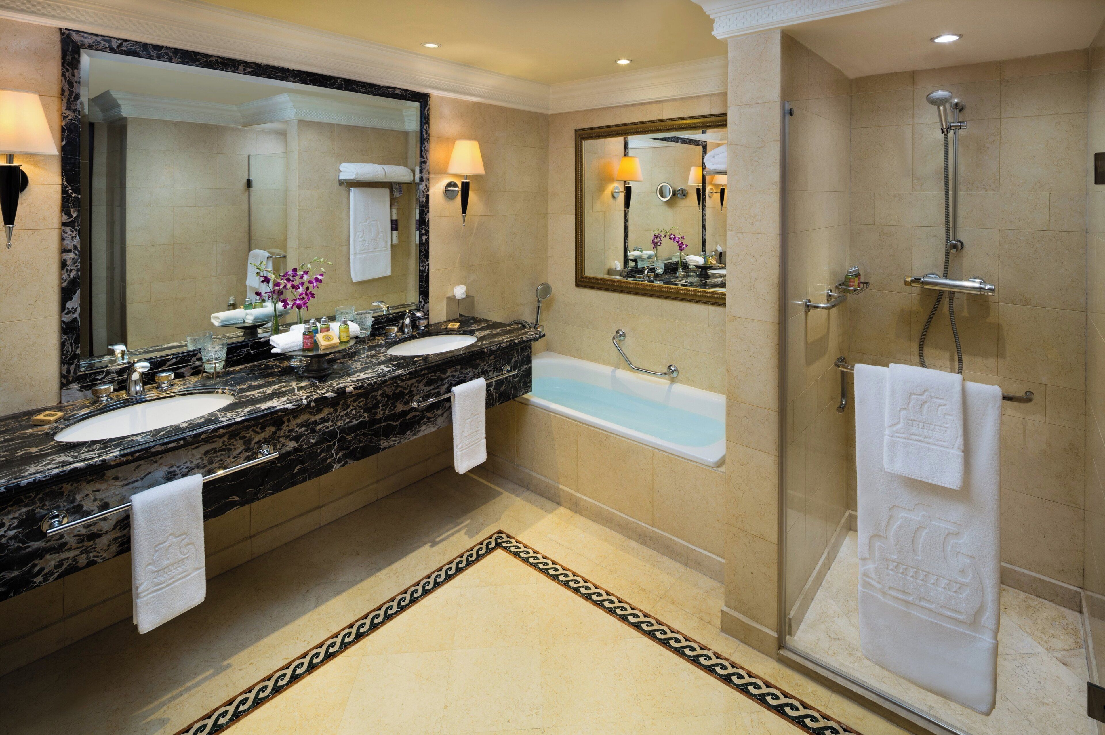 A hotel bathroom with two sinks, a bathtub, and a shower.