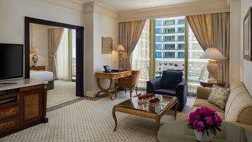 A hotel room with a large bed, a desk with a computer, a TV, a coffee table with flowers, and a view of the city.