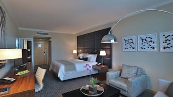 A hotel room with a bed, a desk with a lamp, a chair, a sofa, and artwork on the wall.