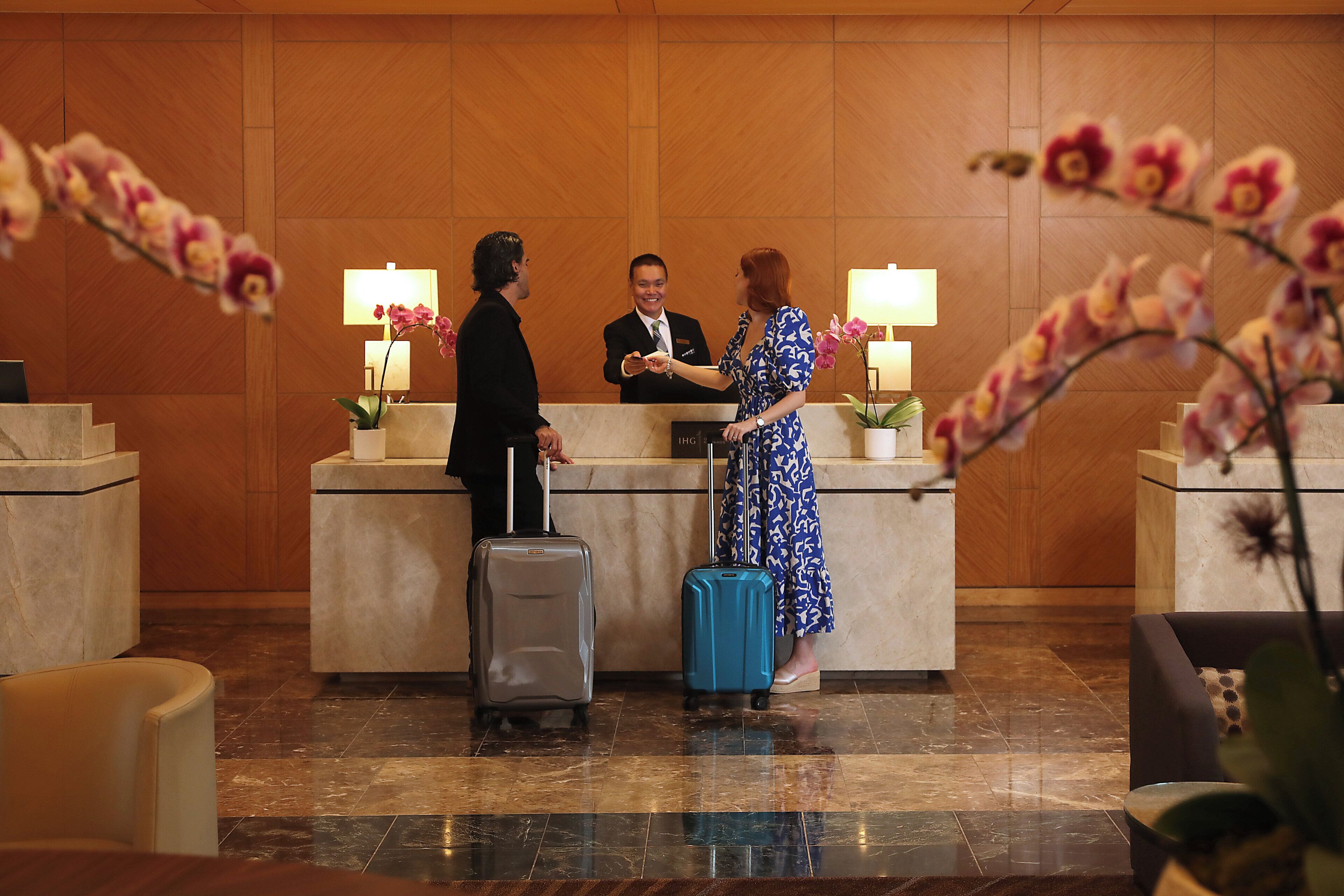 A reception desk with a man and a woman standing, one holding a suitcase.