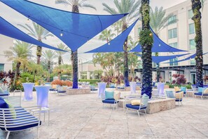 Un área de estar al aire libre con sombrillas azules, sillas blancas y palmeras.