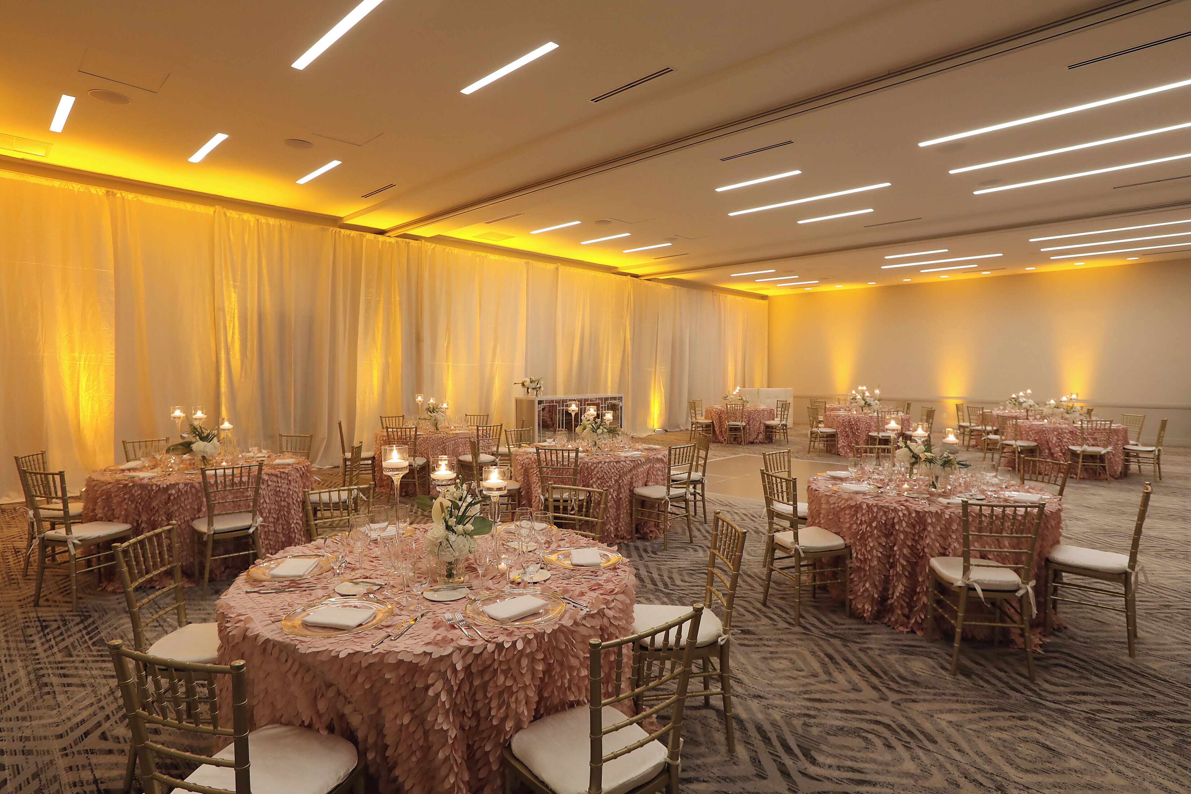 Een feestzaal met ronde tafels, bedekt met roze tafelkleden, in een ruime opstelling met stoelen.
