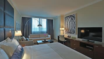 A hotel room with a large bed, a desk, a TV, and a sofa.