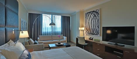 A hotel room with a large bed, a desk, a TV, and a sofa.