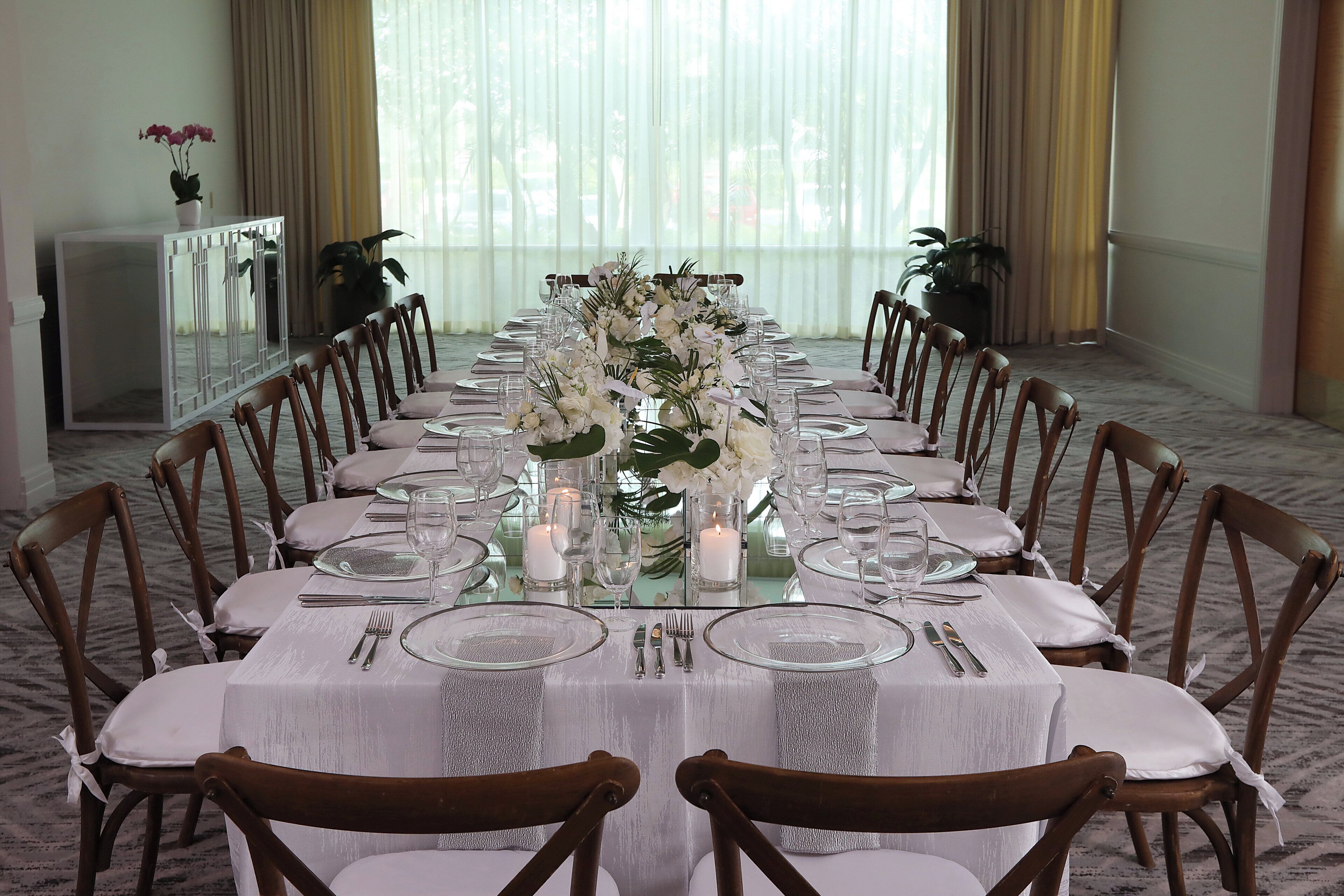 A long dining table set for a formal meal with chairs, glassware, and a centerpiece.