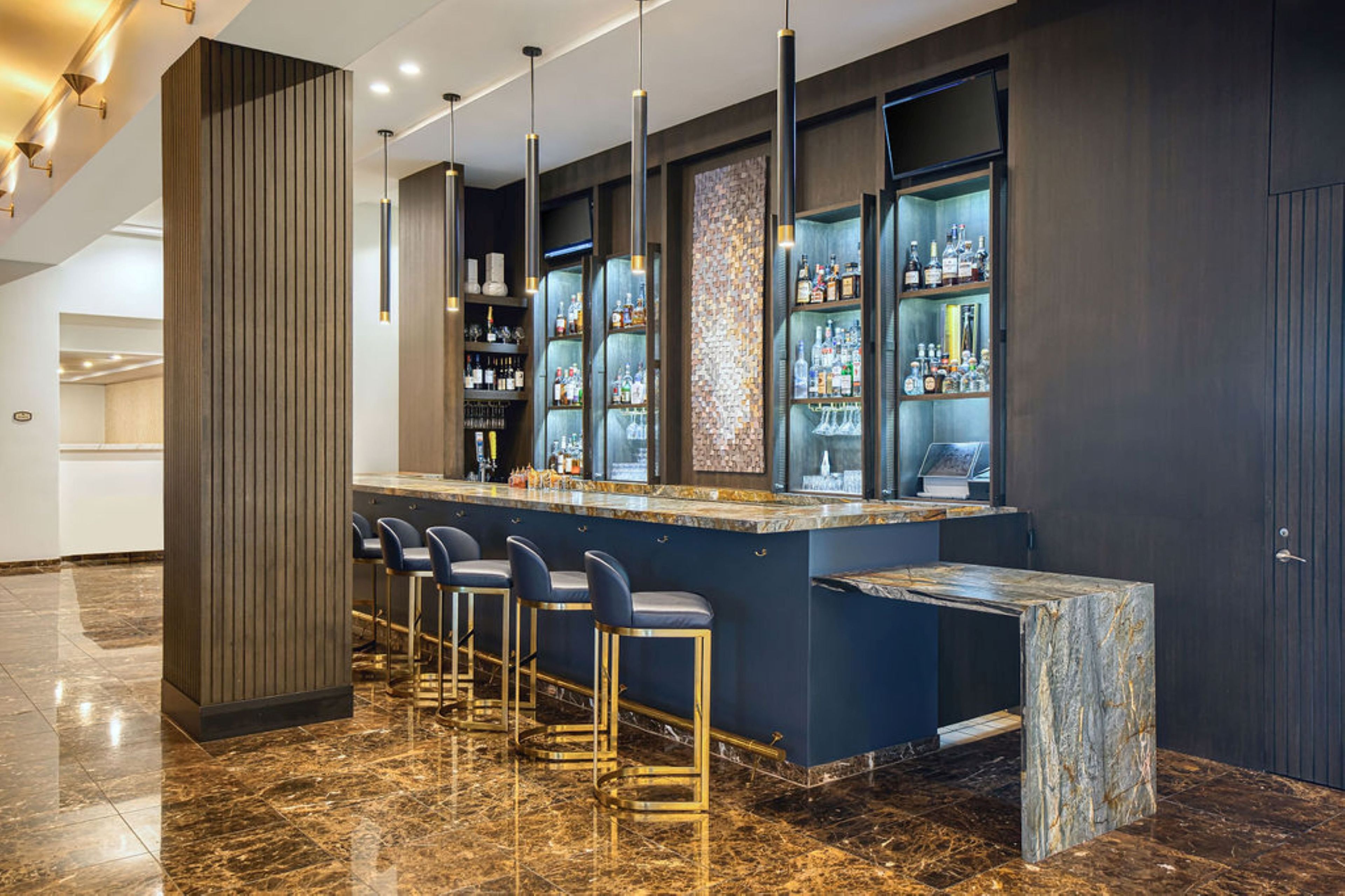 A bar area with a marble countertop, bar stools, and shelves stocked with bottles.