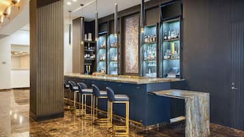 A bar area with a marble countertop, bar stools, and shelves stocked with bottles.