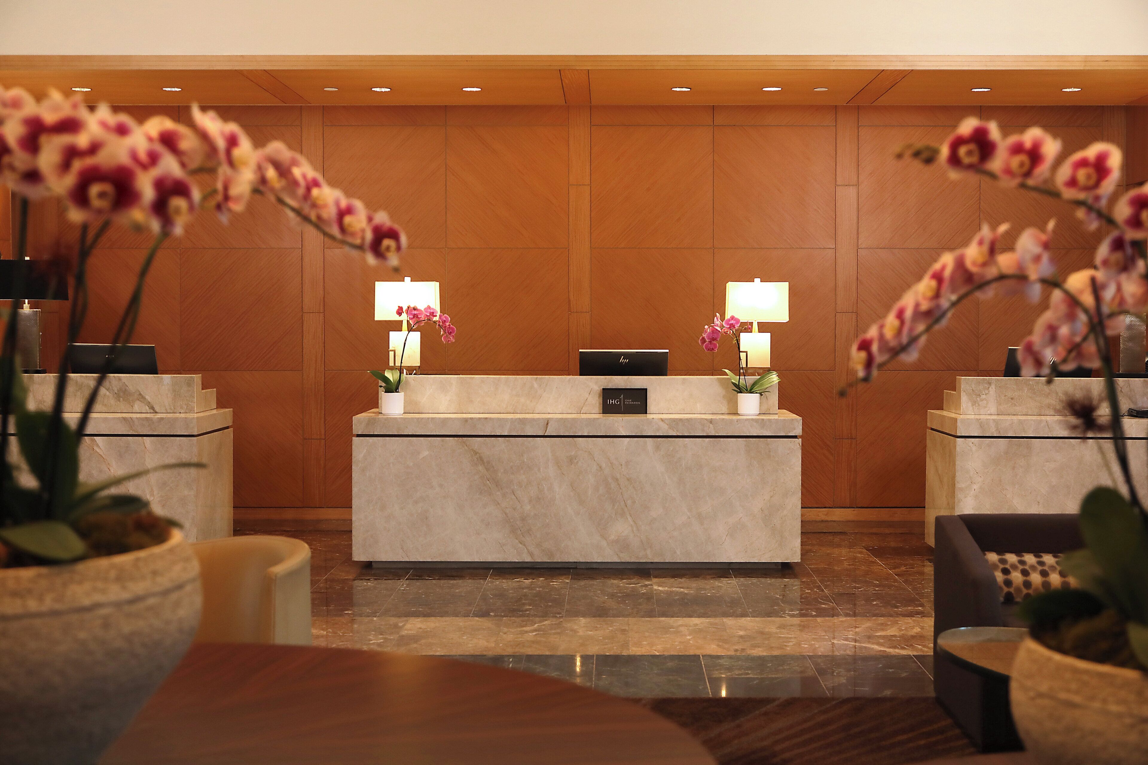 A reception desk with two potted orchids, a reception area with a wooden panel wall, and a marble floor.