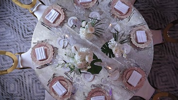 Una mesa redonda con mantel blanco, sillas doradas y un arreglo floral en el centro.
