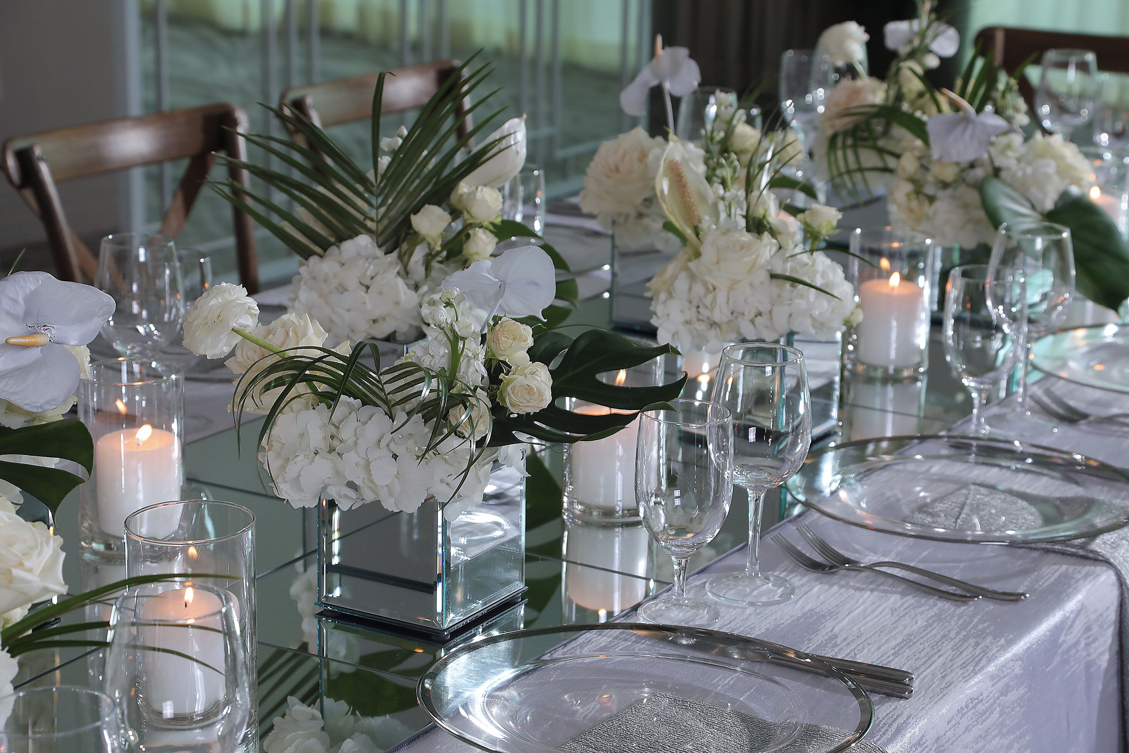 A table set with white flowers, candles, and clear glassware.