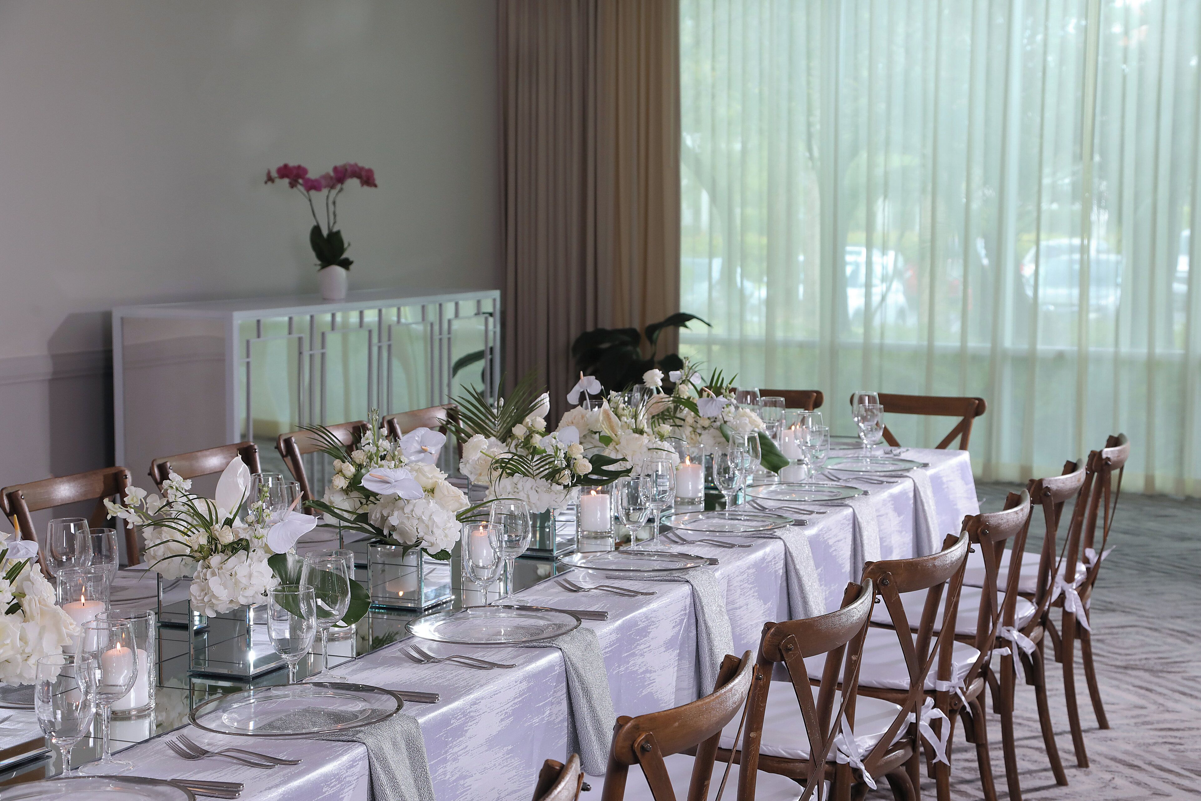 Una larga mesa de comedor dispuesta con manteles blancos, cristalería y centros de mesa florales.