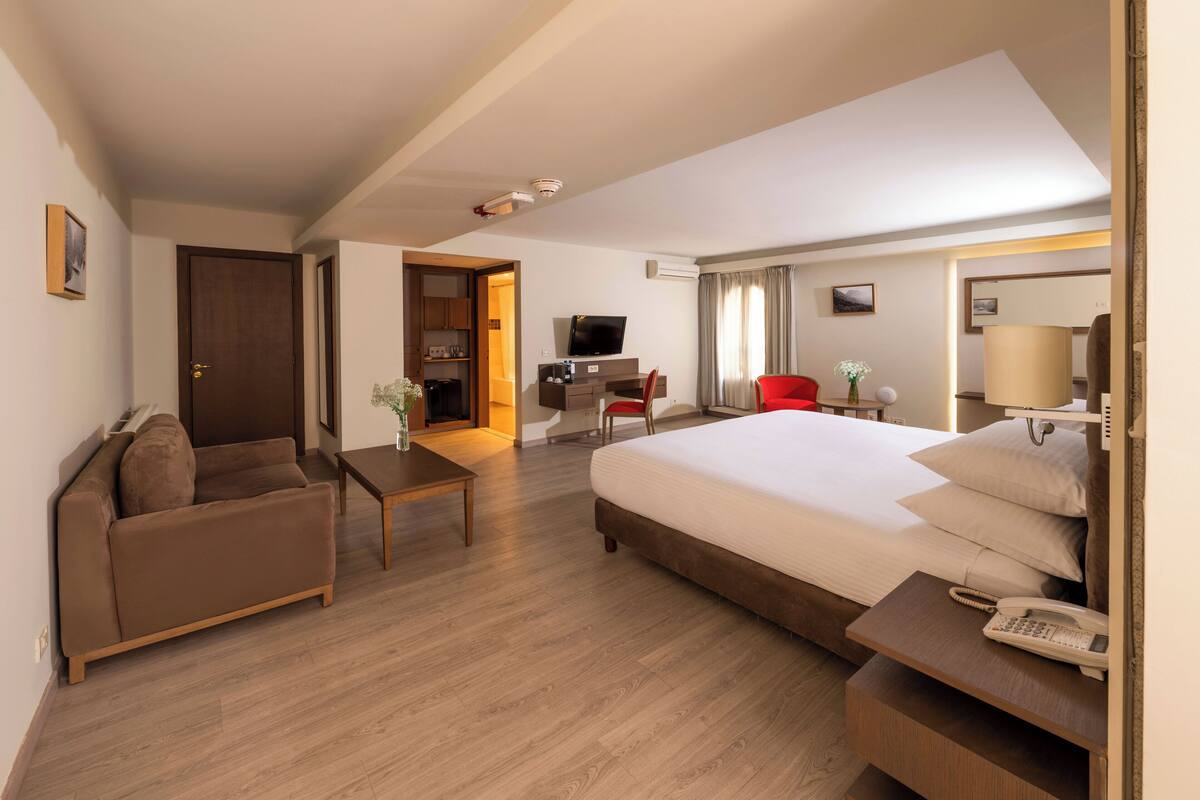 A hotel room with a bed, a sofa, a desk with a computer, a TV, and a phone.