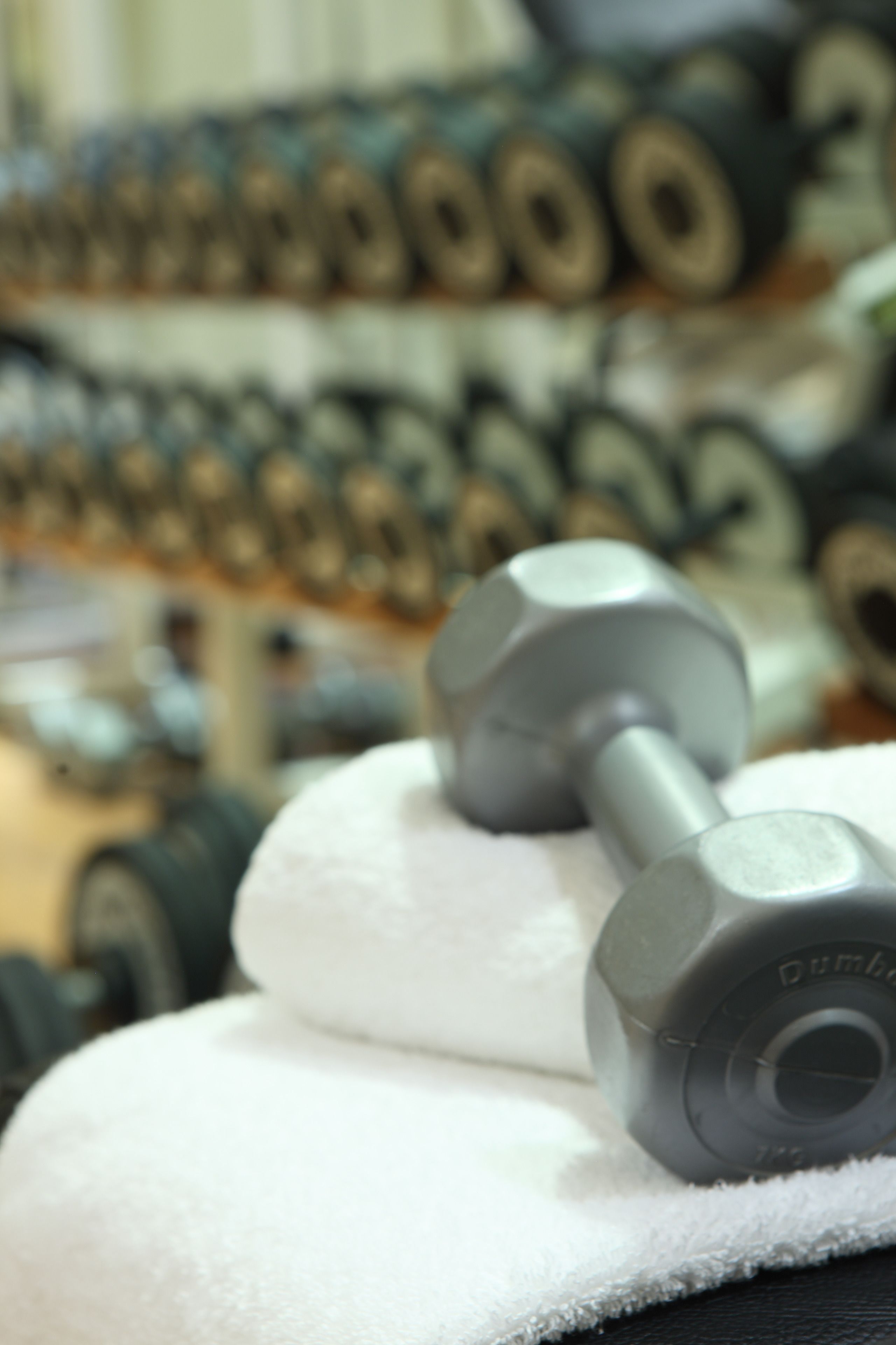 A close-up of a dumbbell on a white towel, with a blurred background of similar dumbbells.