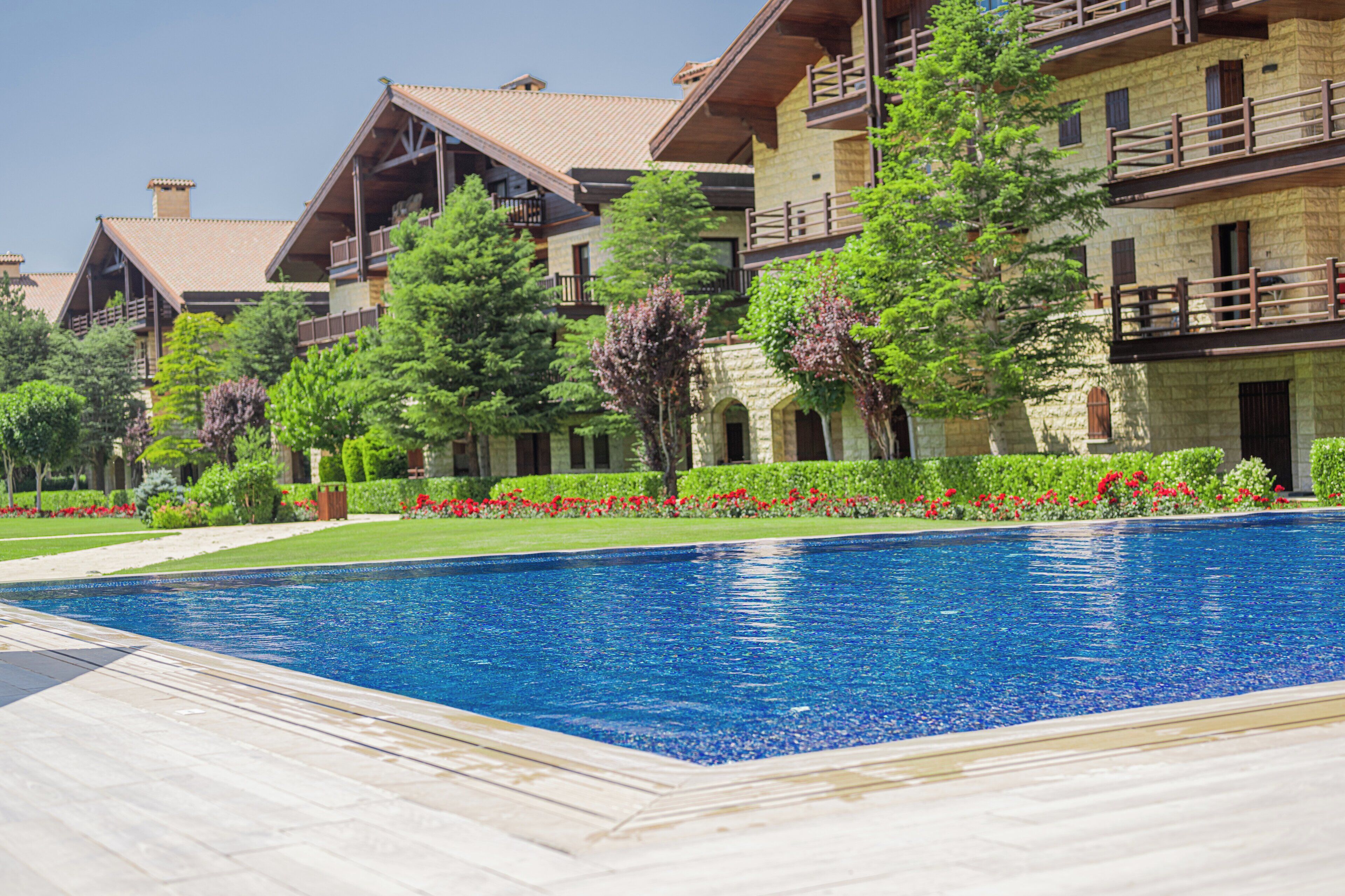 A pool area with a clear blue pool, surrounded by a wooden deck and a stone building with multiple balconies.
