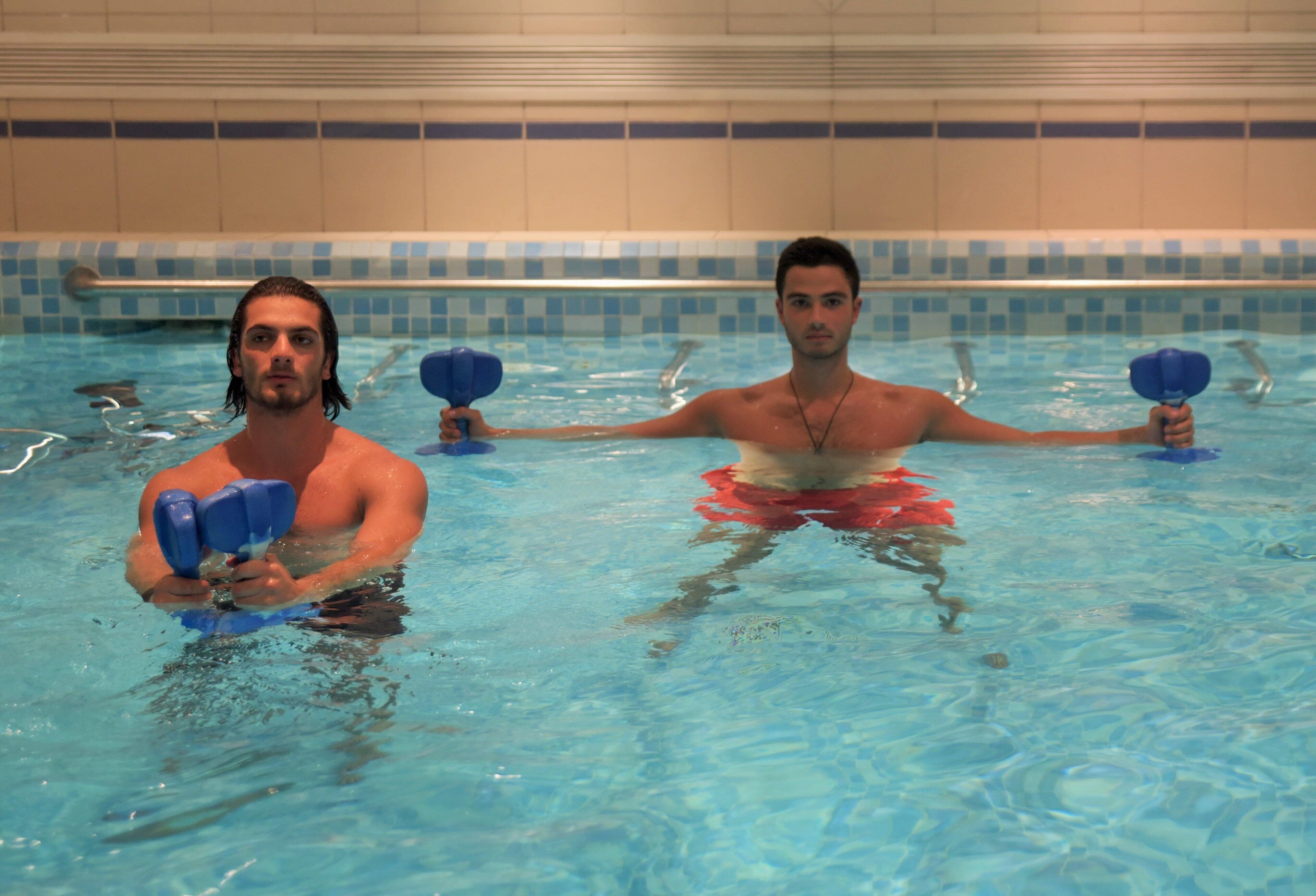 Deux personnes dans une piscine dont les murs sont recouverts de carreaux et dont le bord est bien visible.