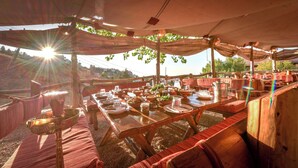 An outdoor dining area with wooden tables and benches, covered by a canopy, and surrounded by greenery. - InterContinental Mzaar Lebanon by IHG (Mzaar Kfardebian)