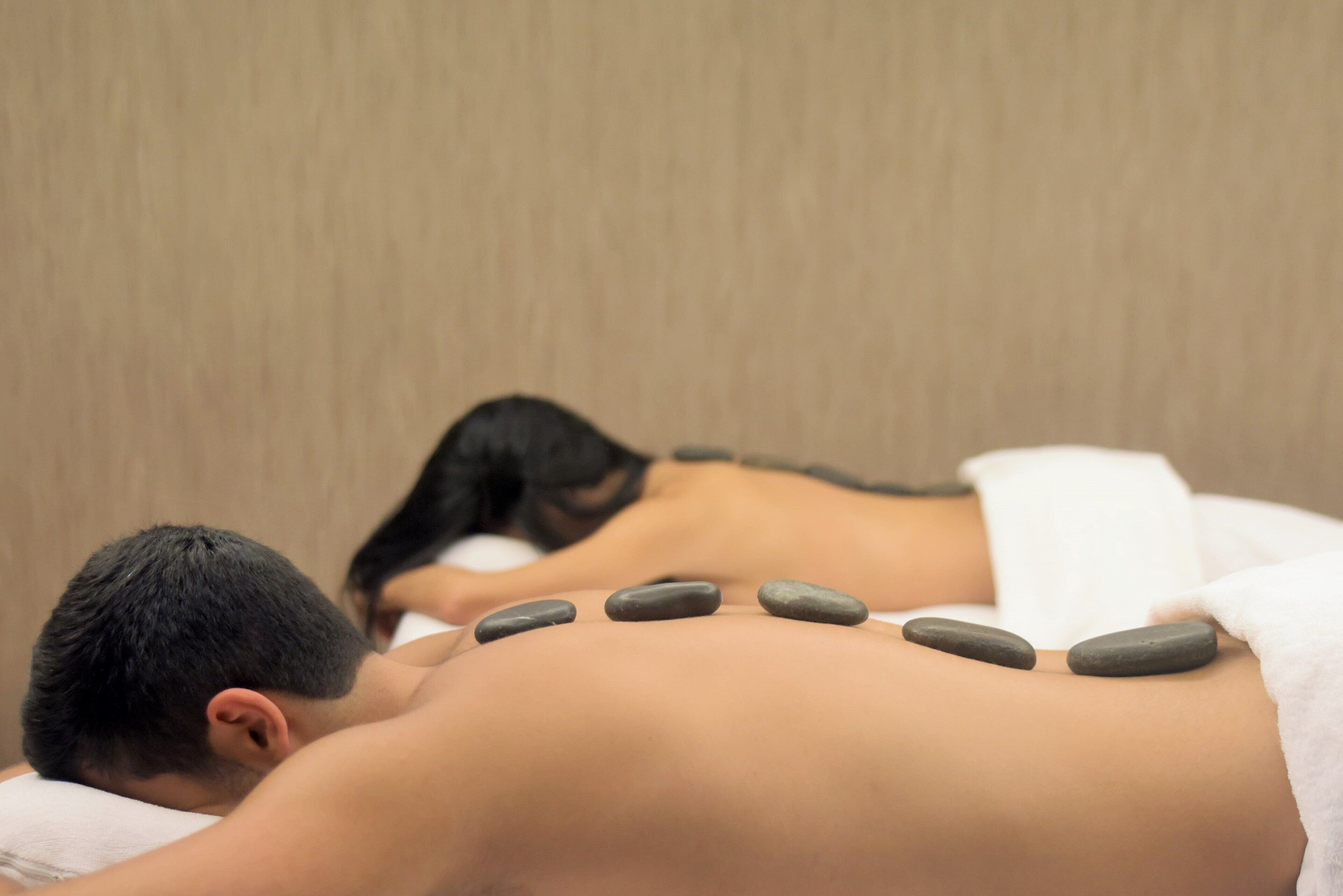 A massage therapy session with a person lying face down, receiving a back treatment with heated stones.
