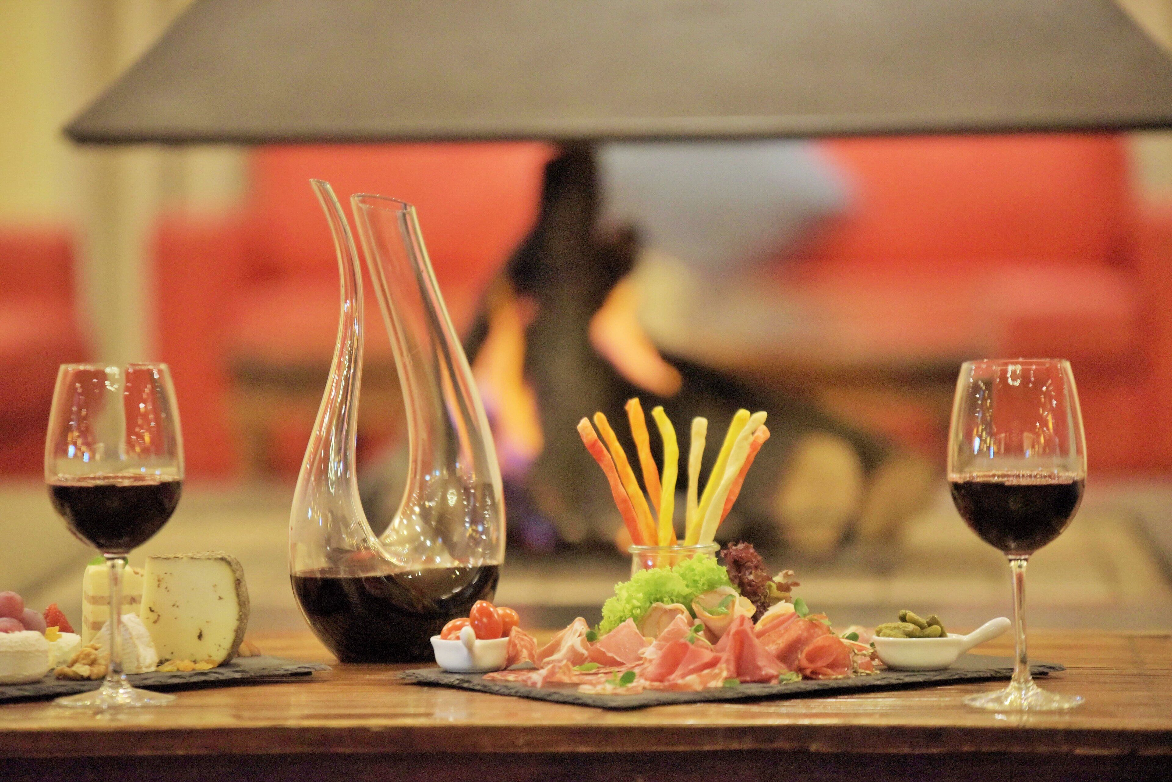 A dining table with wine glasses, a clear glass vase, and a variety of food items including meats and vegetables.