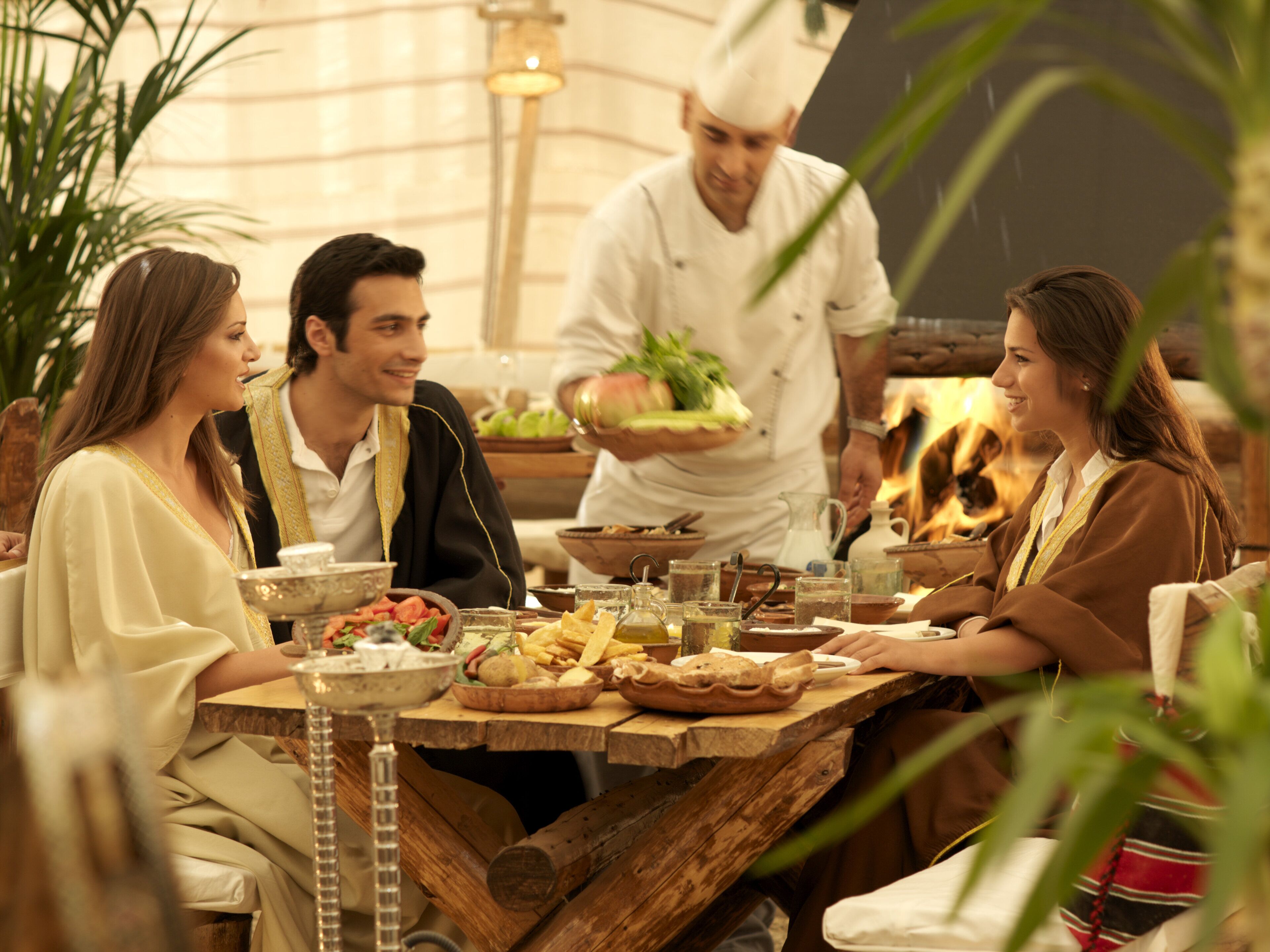 A group of people dining at a wooden table with various dishes and drinks.