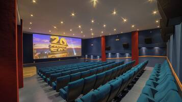 Una sala cinematografica con file di sedie blu, uno schermo grande che mostra un festival cinematografico e un moderno design del soffitto.