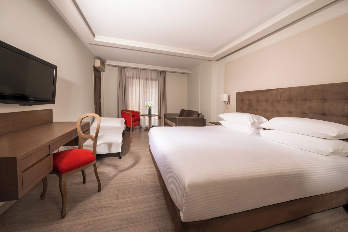 A hotel room with a large bed, a desk, a chair, a television, and a window with curtains.