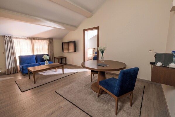 A modern living room with a blue sofa, a wooden coffee table, a round dining table with a blue chair, and a large mirror.