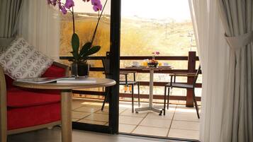 A room with a red sofa, a small table with a vase of flowers, and a balcony with a view of the countryside.