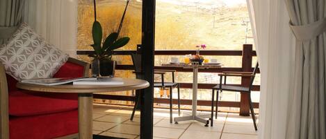 Una habitación con un sofá rojo, una mesita con un jarrón de flores y un balcón con vistas al campo.