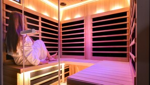 A sauna with wooden benches and slatted walls, a person sitting on one of the benches, and a small table in front. - InterContinental Mzaar Lebanon by IHG (Mzaar Kfardebian)