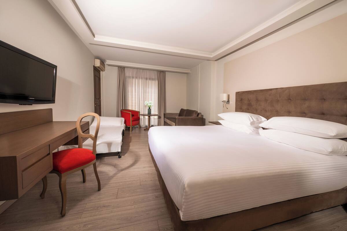 A hotel room with a large bed, a desk, a chair, a television, and a window with curtains.