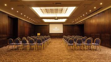 A conference room with rows of chairs, a projector screen, and a ceiling with recessed lighting.