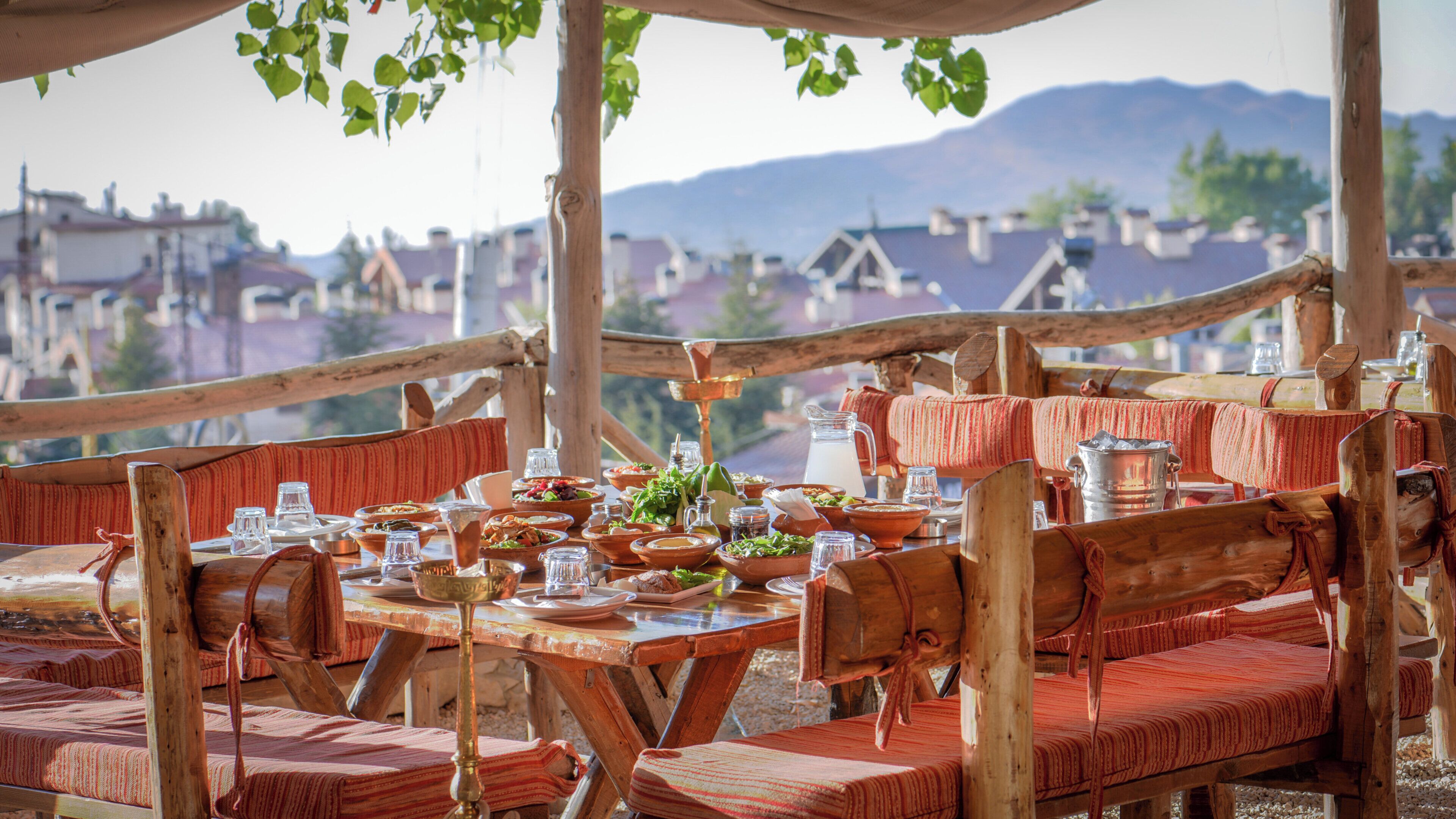 Un espace extérieur aménagé pour les repas, avec du mobilier en bois et une vue sur la ville et les montagnes en arrière-plan.