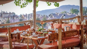An outdoor dining area with wooden furniture and a view of a town and mountains in the background. - InterContinental Mzaar Lebanon by IHG (Mzaar Kfardebian)