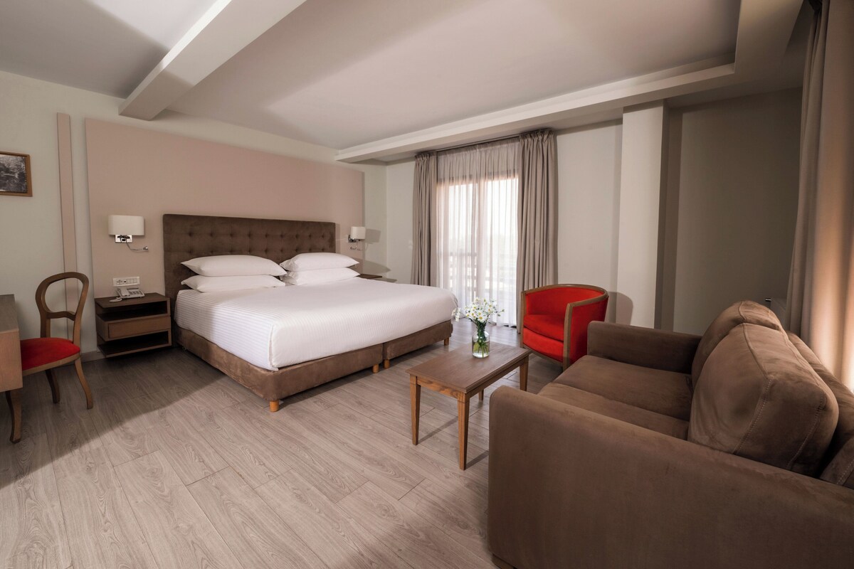 A hotel room with a large bed, a sofa, a coffee table, and a desk.