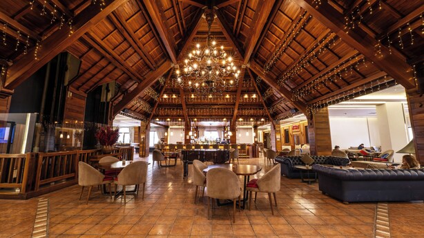A spacious interior with a high wooden ceiling, a central bar area, multiple seating arrangements, and a chandelier. - InterContinental Mzaar Lebanon by IHG (Mzaar Kfardebian)