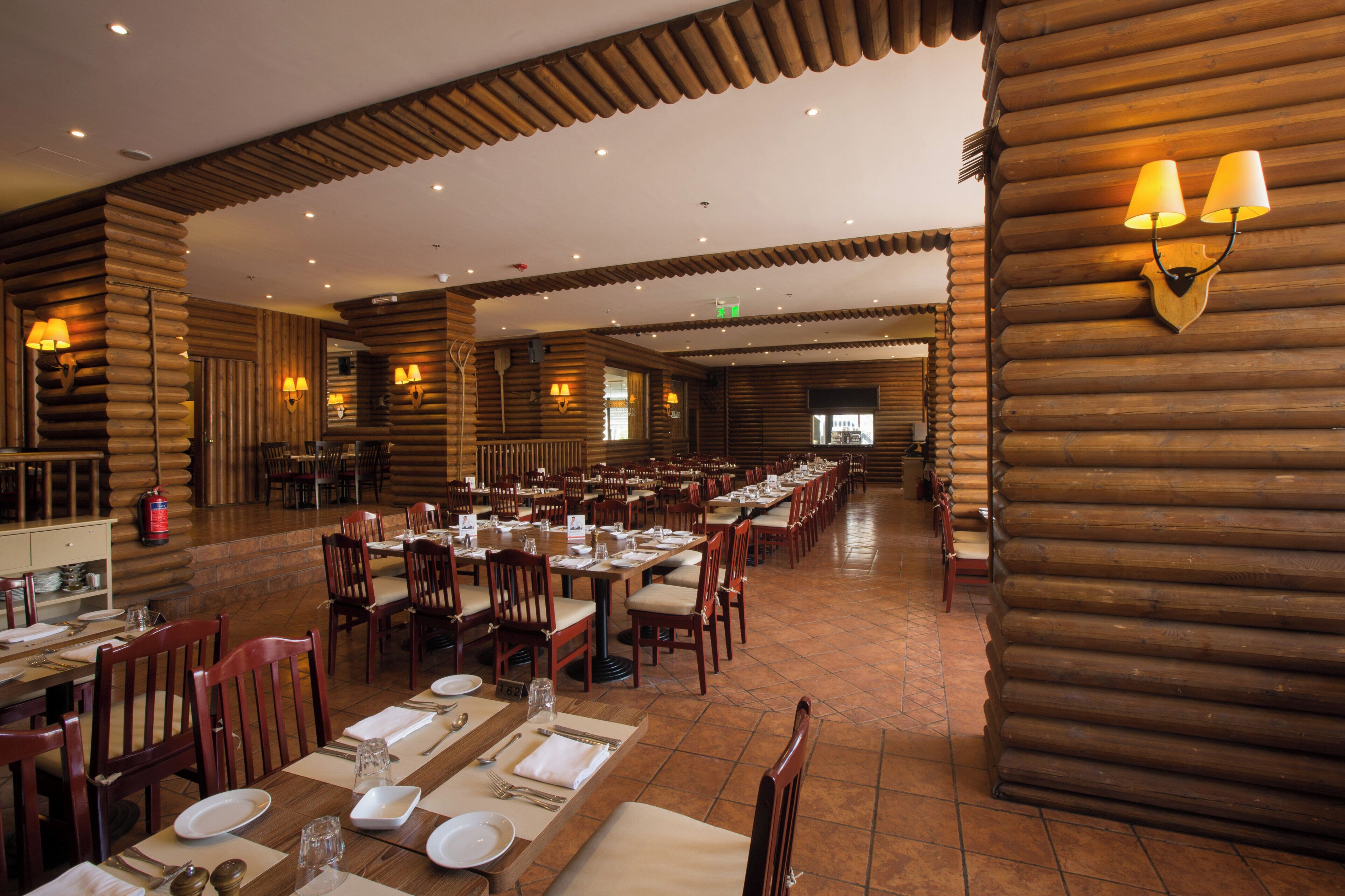 Un comedor amplio con varias mesas y sillas, paredes de madera e iluminación empotrada.