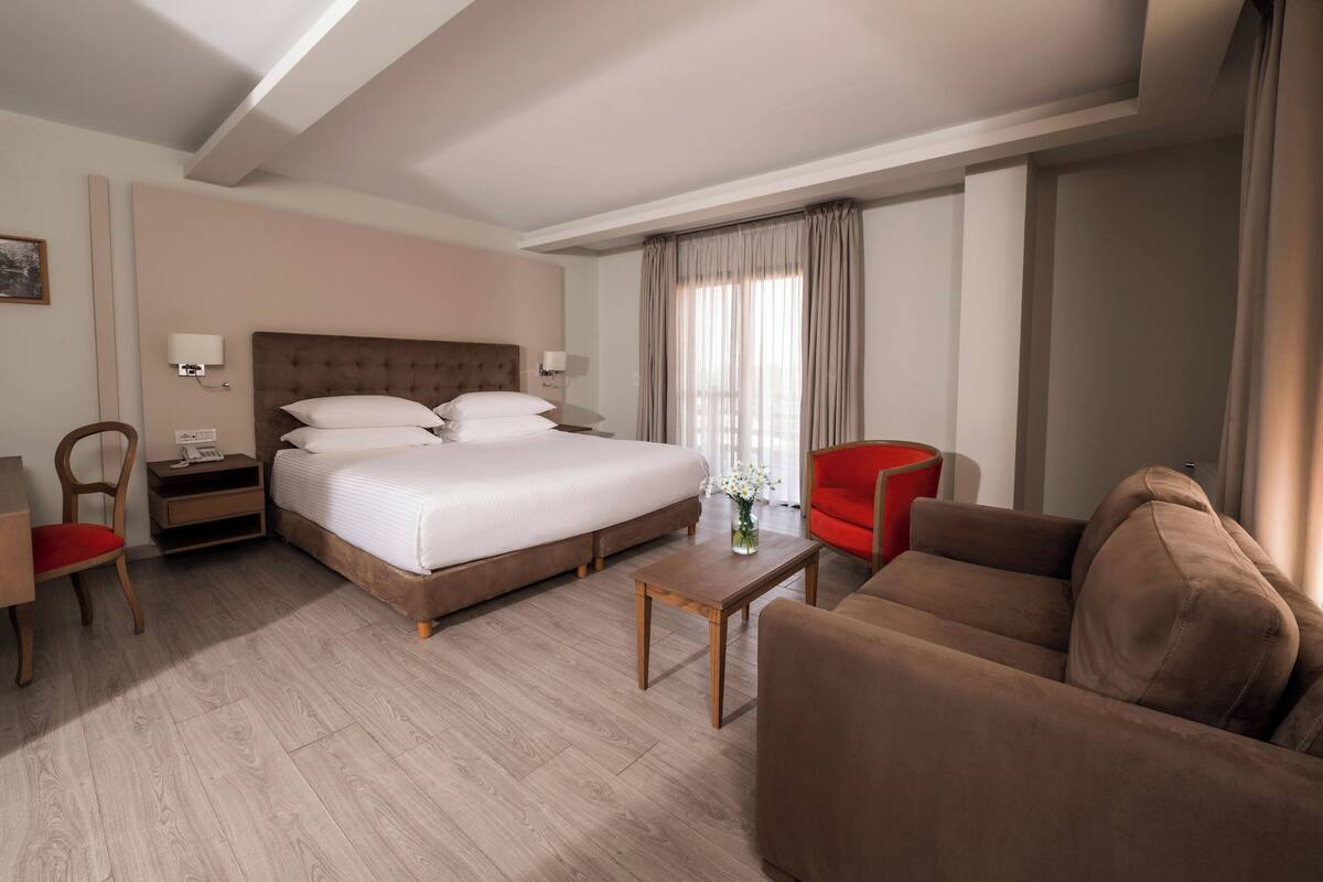 A hotel room with a large bed, a sofa, a coffee table, and a desk.