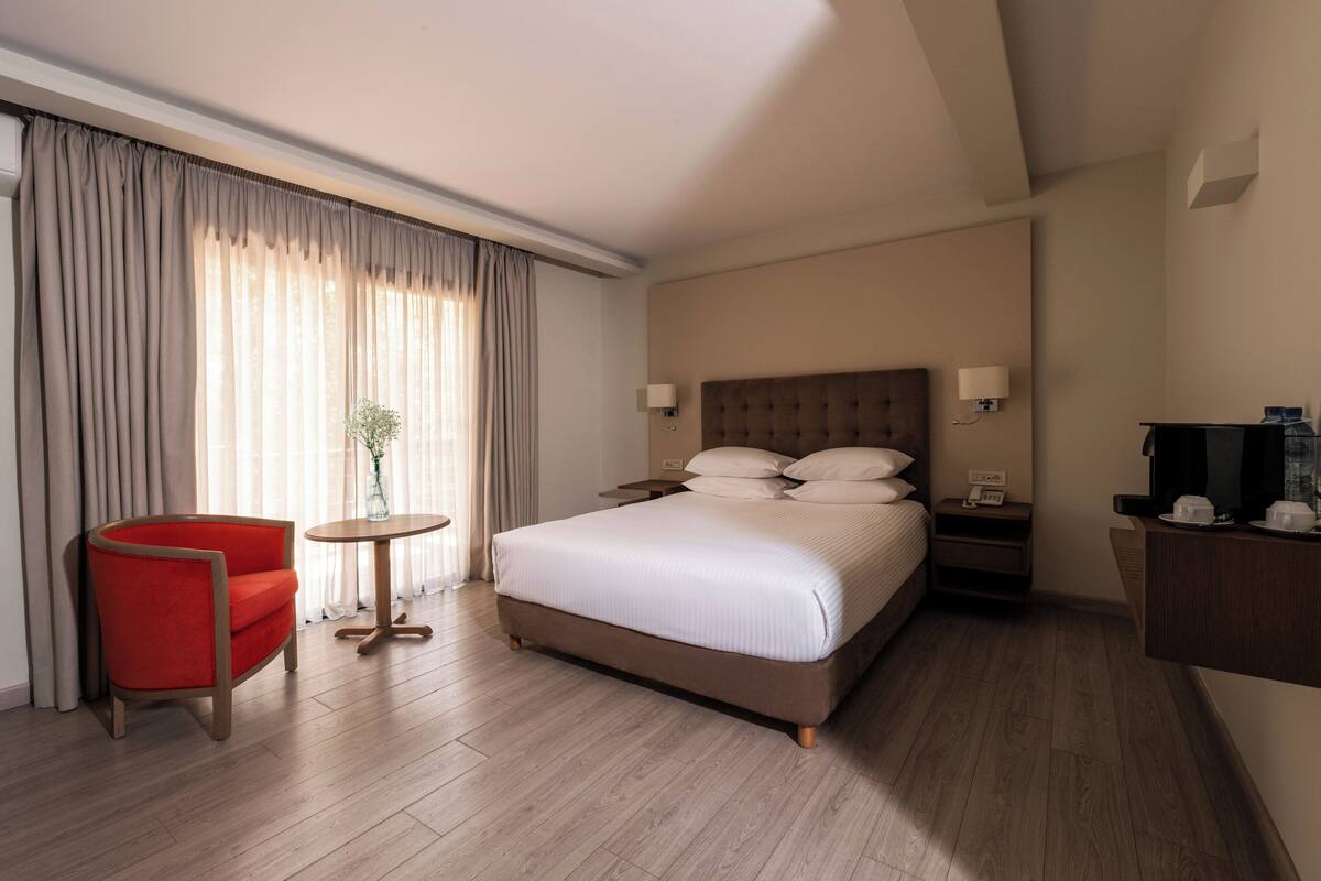 A hotel room with a large bed, a red armchair, a small round table, and a TV on a wooden stand.