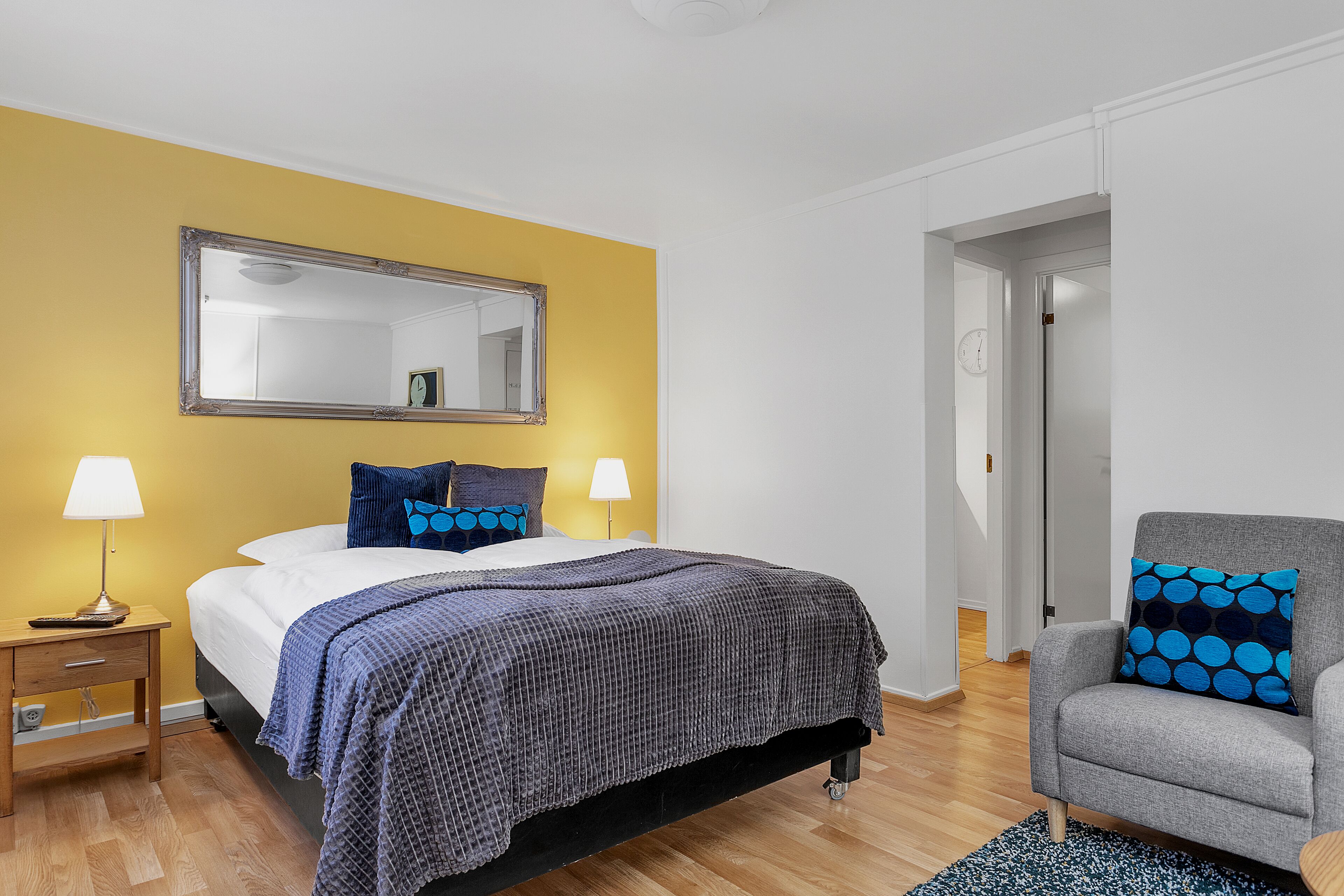 A bedroom with a bed, bedside lamps, a chair, and a mirror.