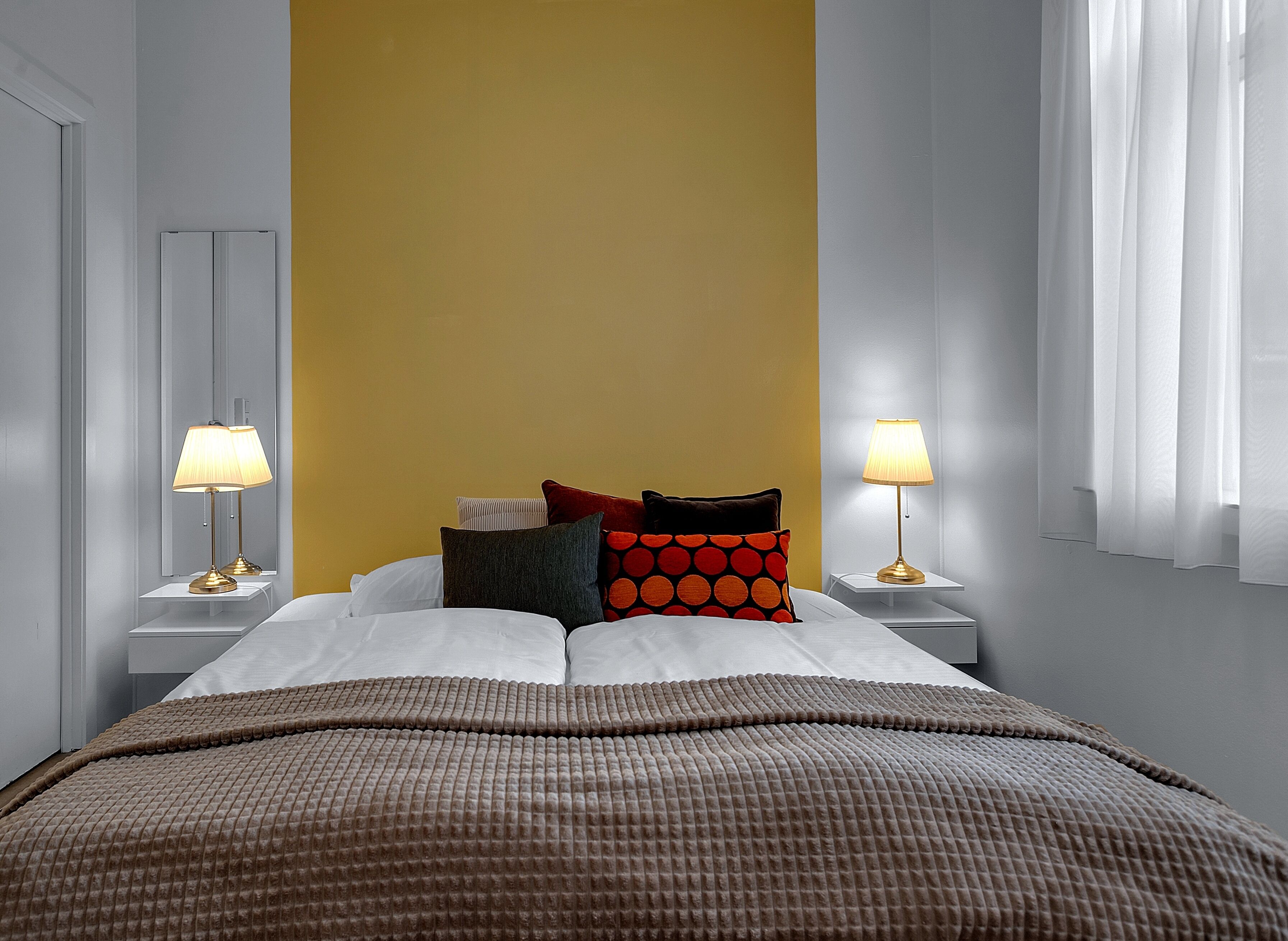 Una camera d'albergo con un letto, due lampade ai comodini e una parete gialla.