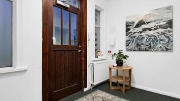 Un couloir avec une porte en bois, un radiateur, une œuvre d’art encadrée et une petite table sur laquelle se trouve une plante.