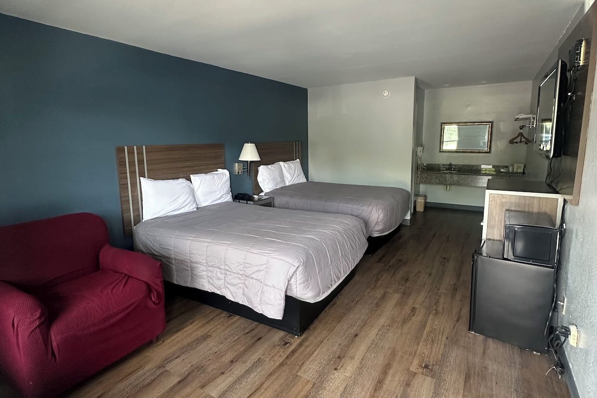 Una habitación de hotel con una cama, una silla roja, un escritorio y un espejo.