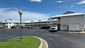 A parking lot with a white building, a lamp post, and a clear blue sky. - Key West Inn - Clanton (Clanton)