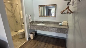 A bathroom with a marble shower, a sink with a mirror, and a wooden floor. - Key West Inn - Clanton (Clanton)