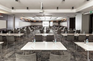 A conference room with multiple tables and chairs, equipped with water bottles and nameplates, and a projector screen displaying "nippon hotel".