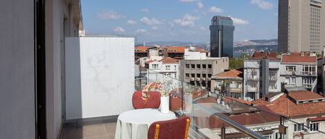 Un balcón con mesa y sillas, con vistas a un paisaje urbano con diversos edificios y un cielo despejado.